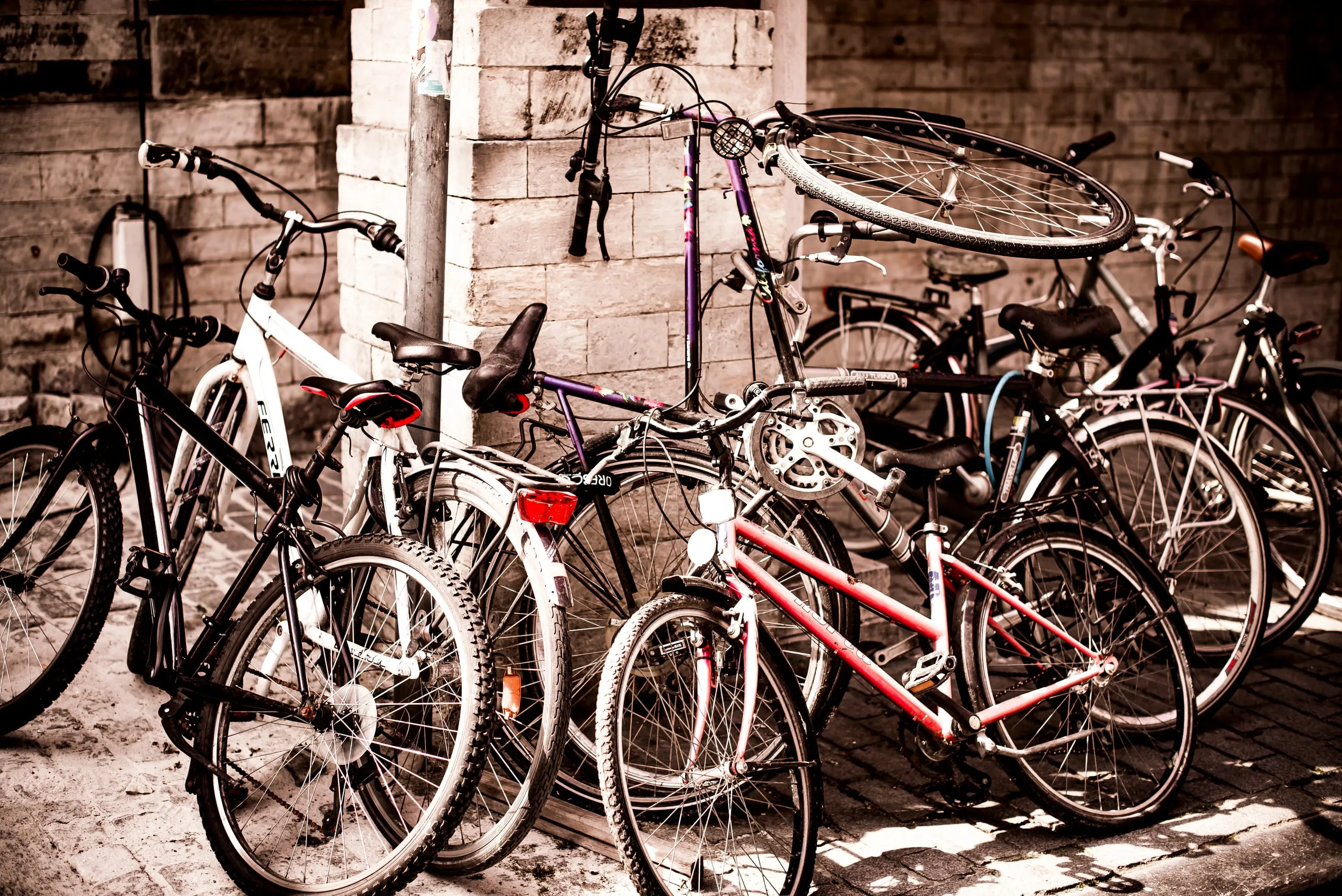 Een kluwen geparkeerde fietsen tegen een bakstenen muur, in warme sepiatinten
