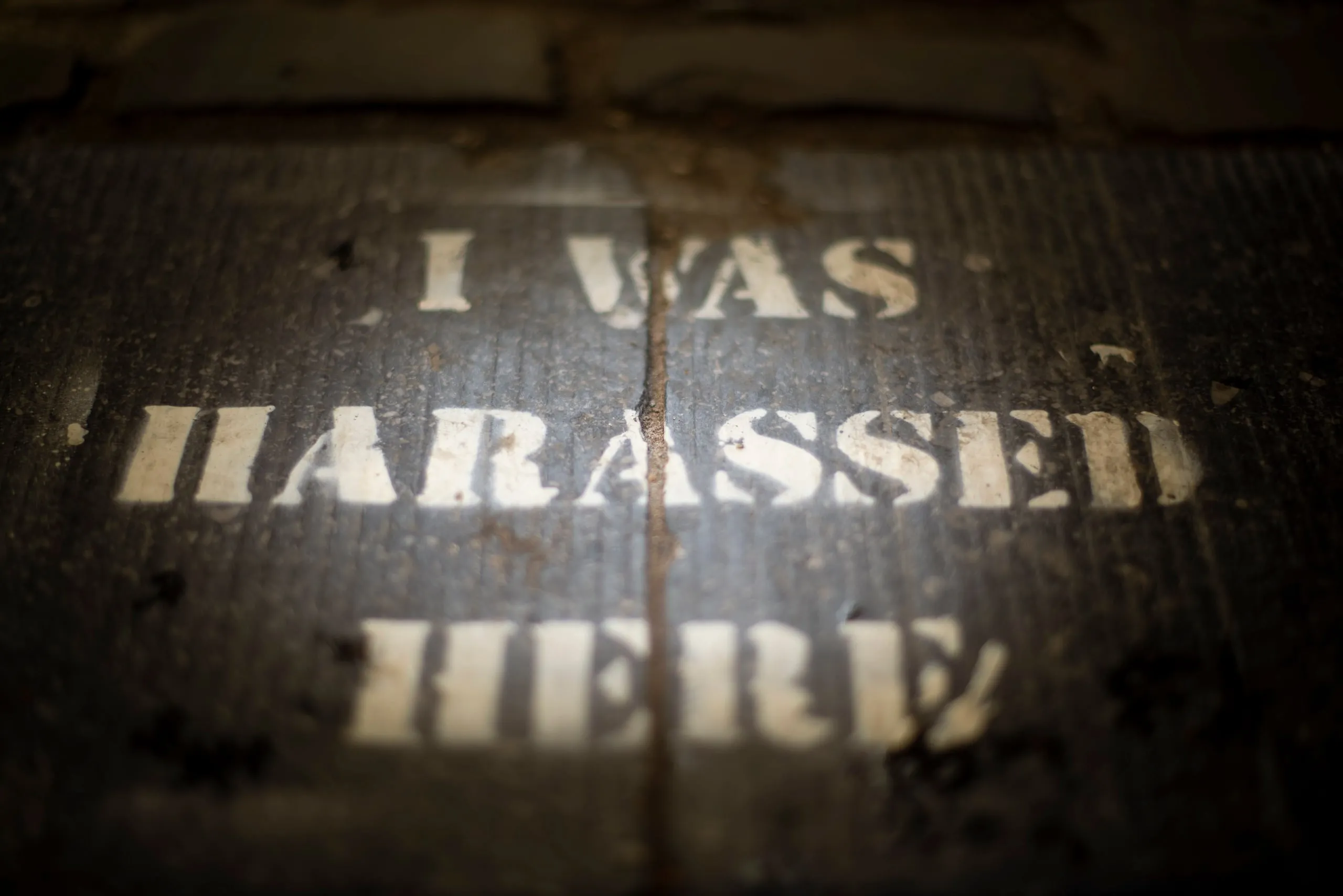 Gestencilde tekst 'I was harassed here' op een donkere stoep