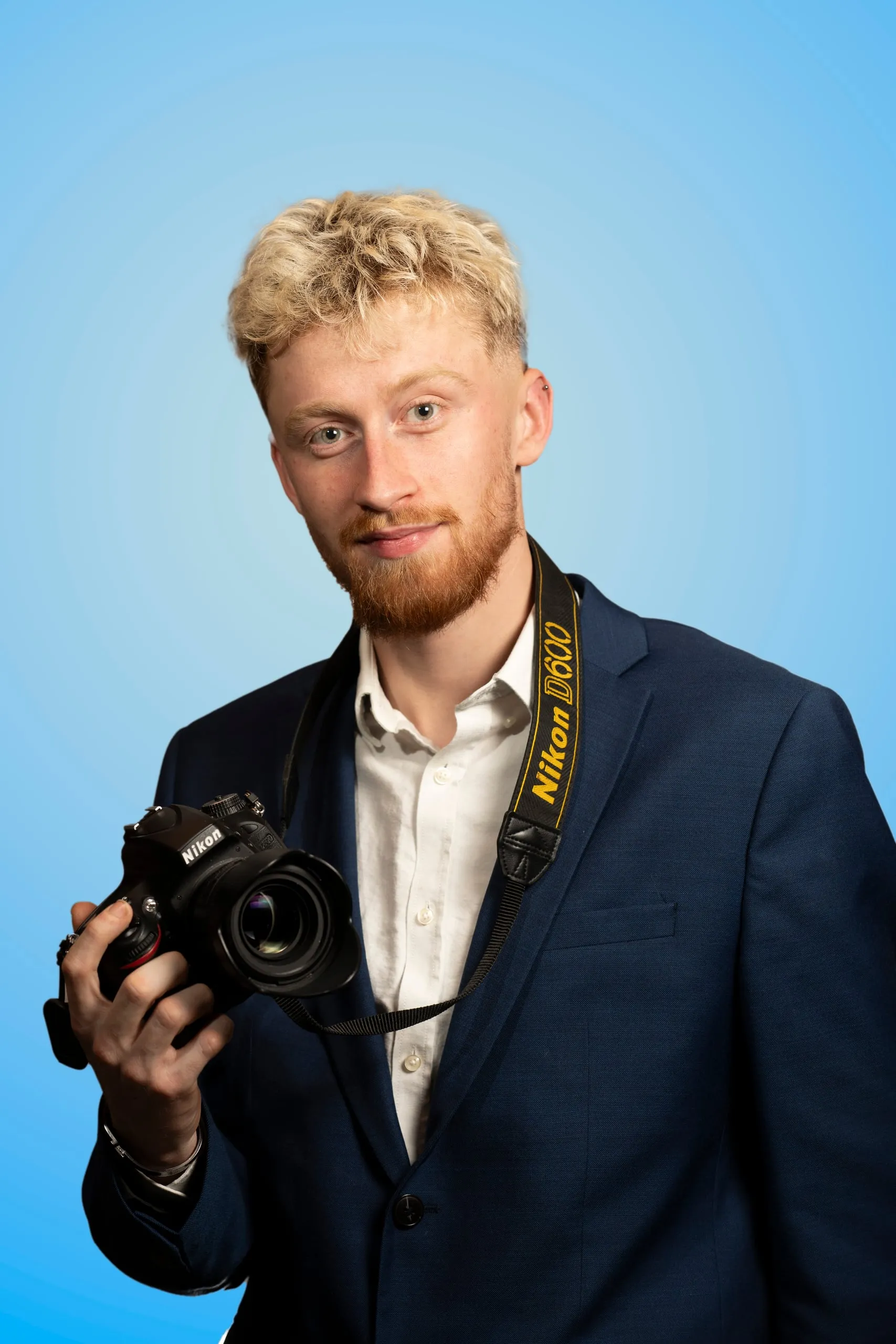 Man in marineblauw pak met een camera in de hand voor een blauwe achtergrond