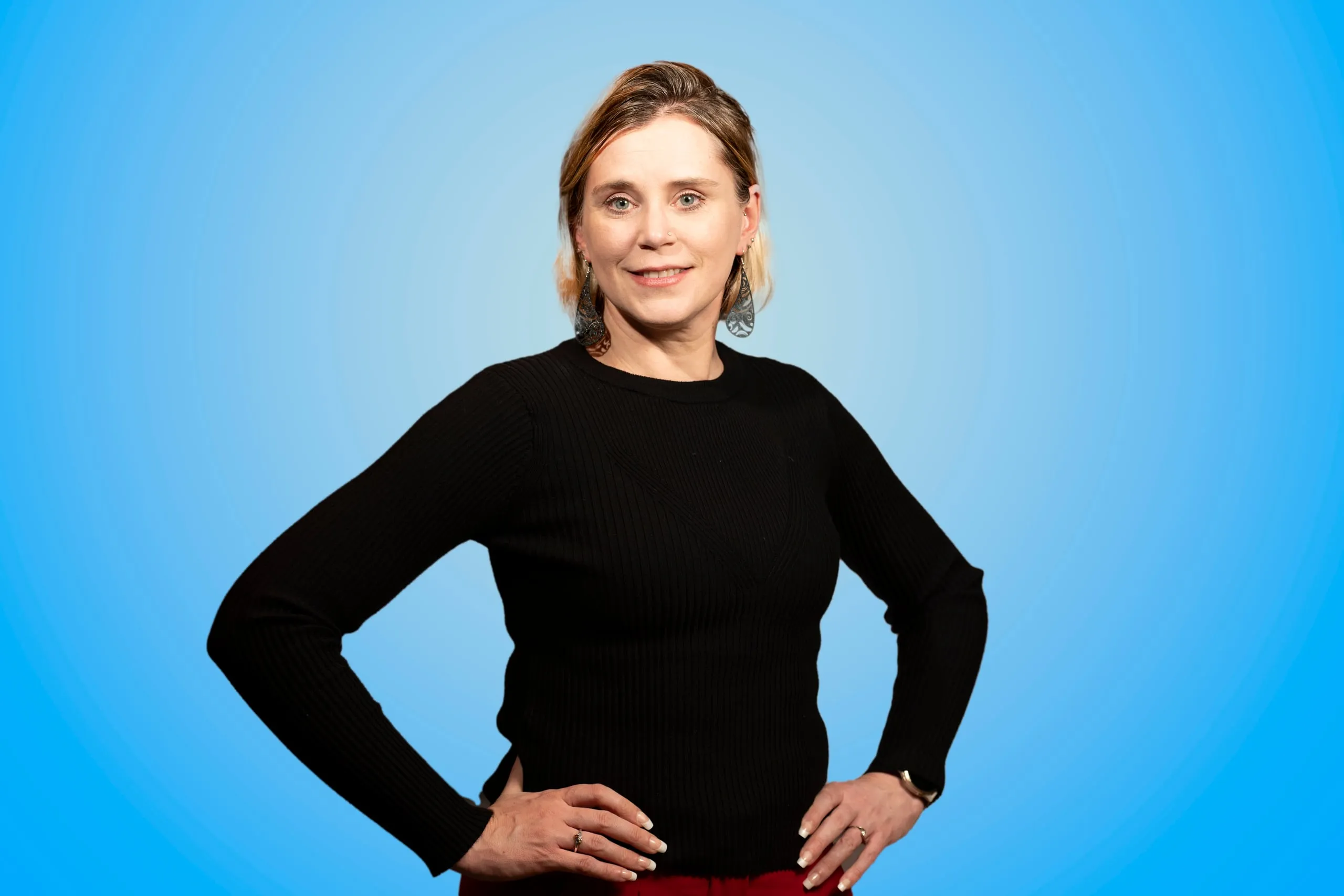 Vrouw in zwarte trui met de handen op de heupen voor een blauwe achtergrond