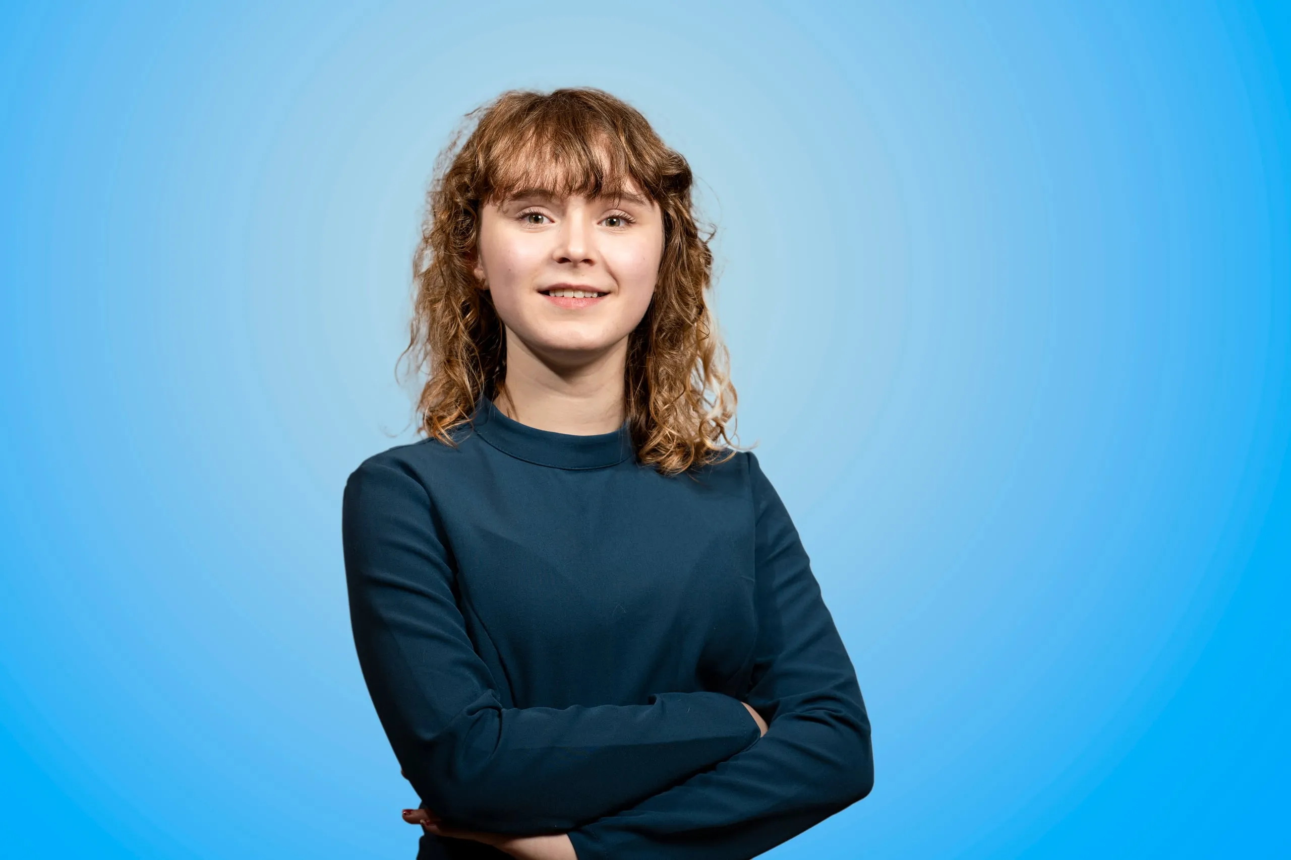 Jonge vrouw met krullend haar in een blauwe jurk met gekruiste armen