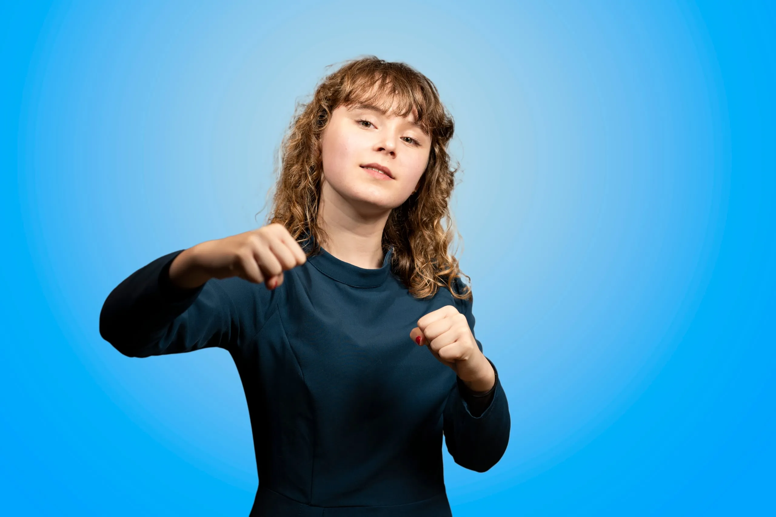 Jonge vrouw met krullend haar in een blauwe jurk met gebalde vuisten in een speelse houding