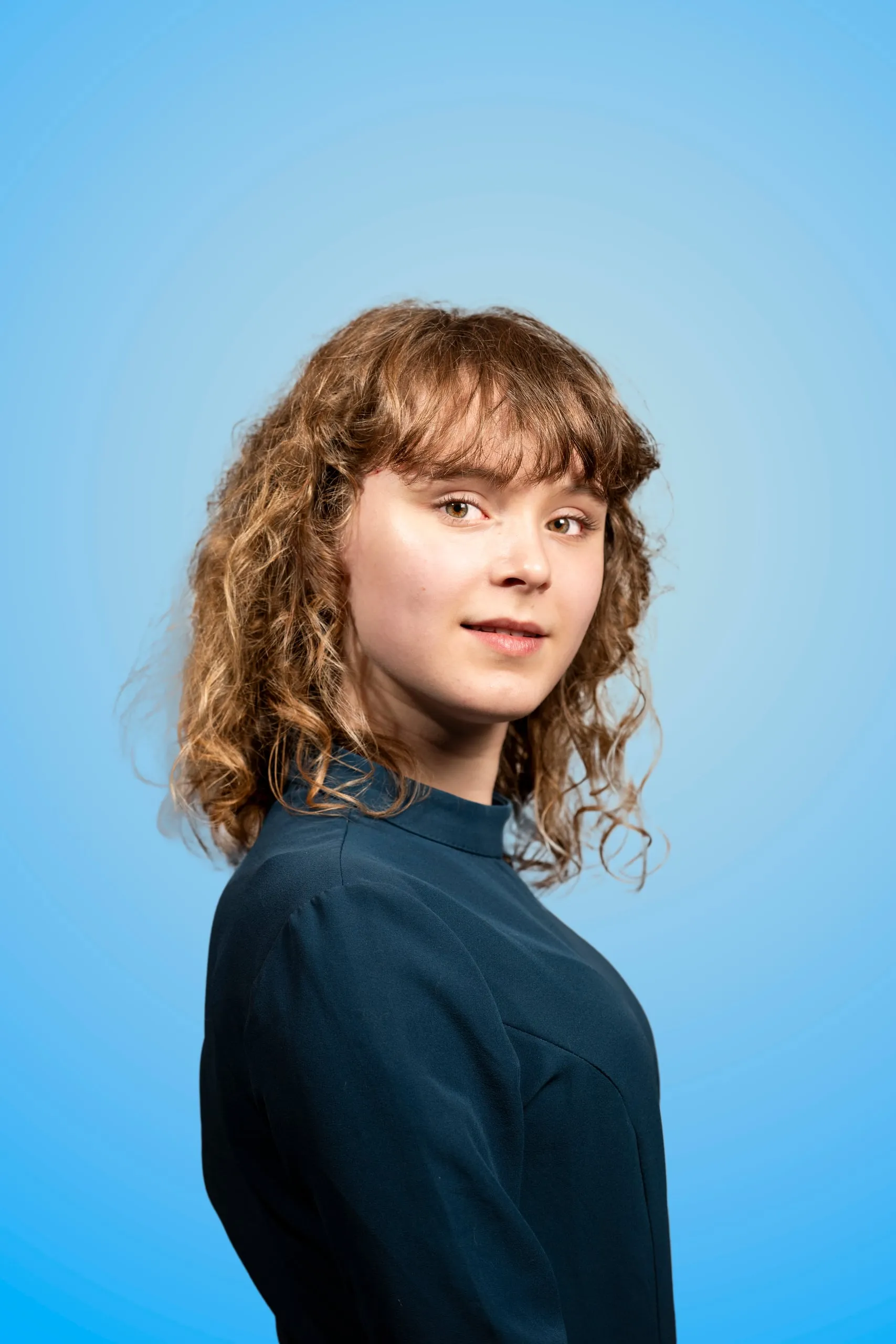 Jonge vrouw met krullend haar kijkt over haar schouder naar de camera