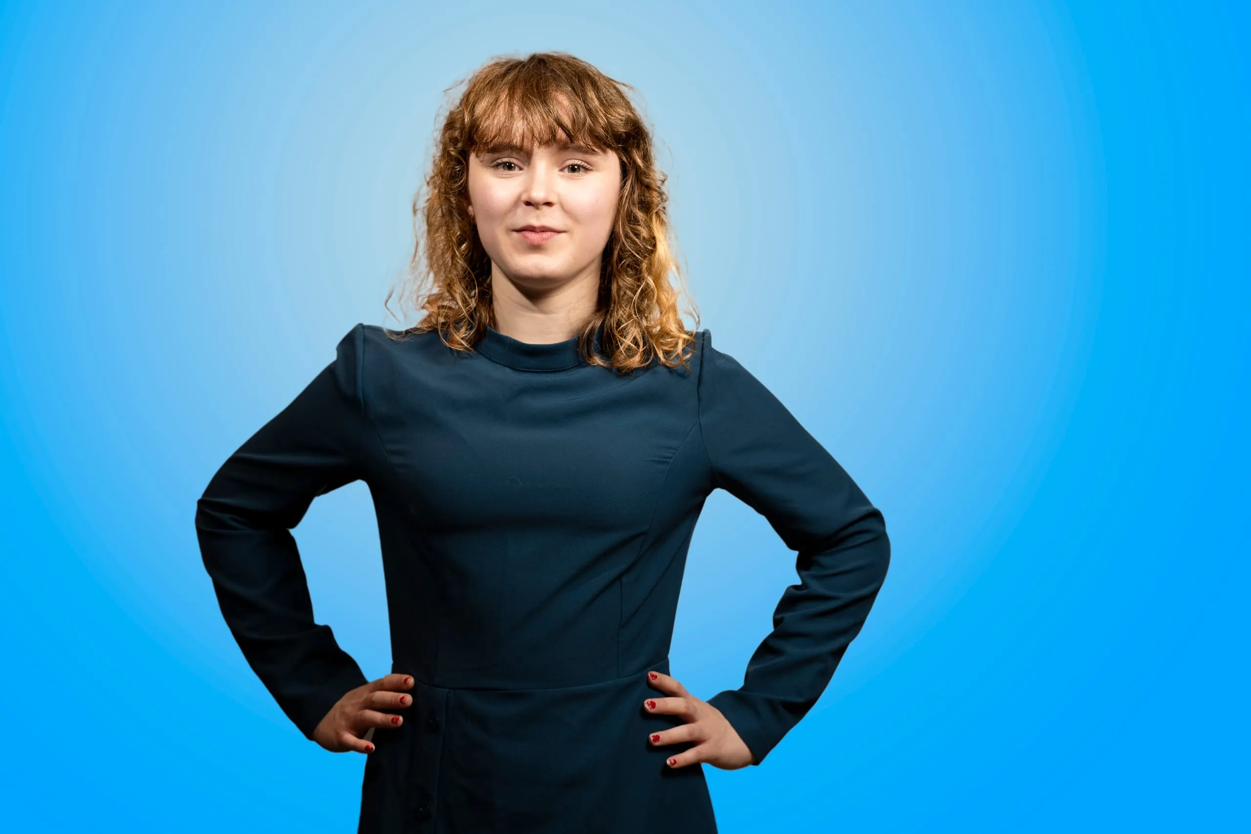 Jonge vrouw in een blauwe jurk met de handen op de heupen