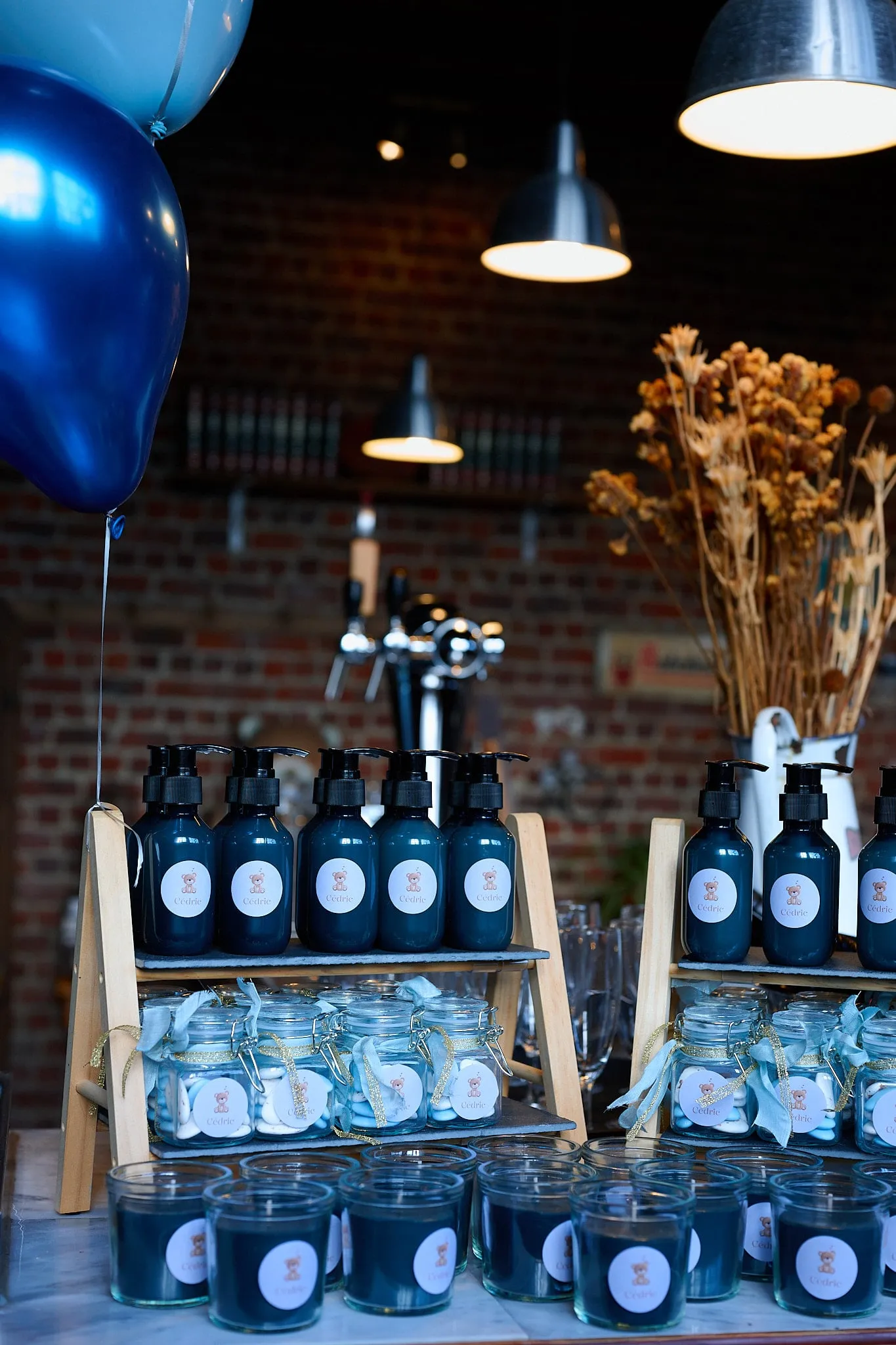 Tafel met donkere zeepflessen, glazen potjes en kaarsen onder blauwe ballonnen