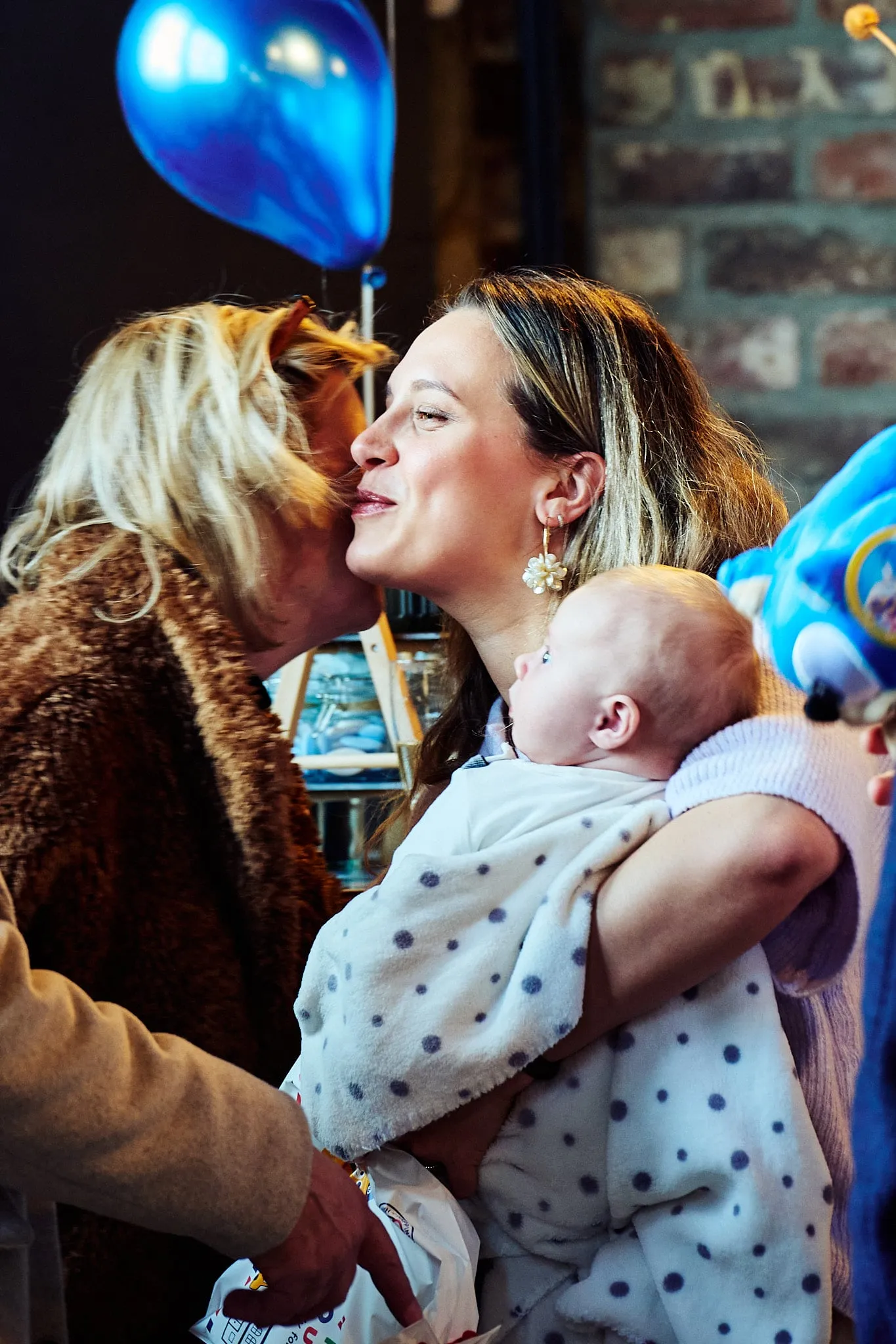 Een gast kust een jonge moeder met baby op de wang