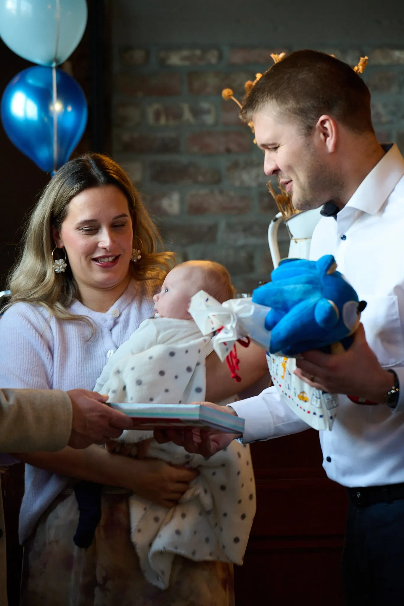 Een man overhandigt een blauw knuffeldier aan een vrouw met een baby