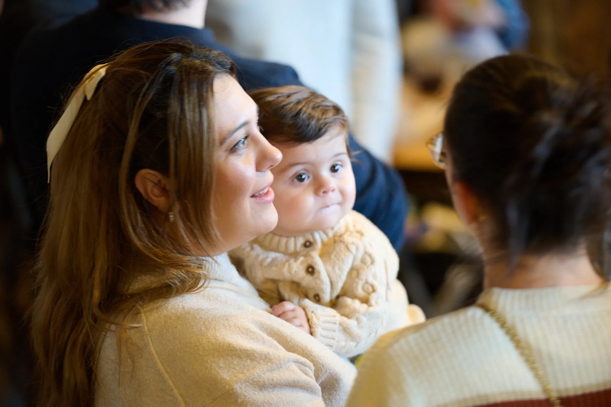 Vrouw met een peuter op schoot kijkt opzij tussen andere gasten