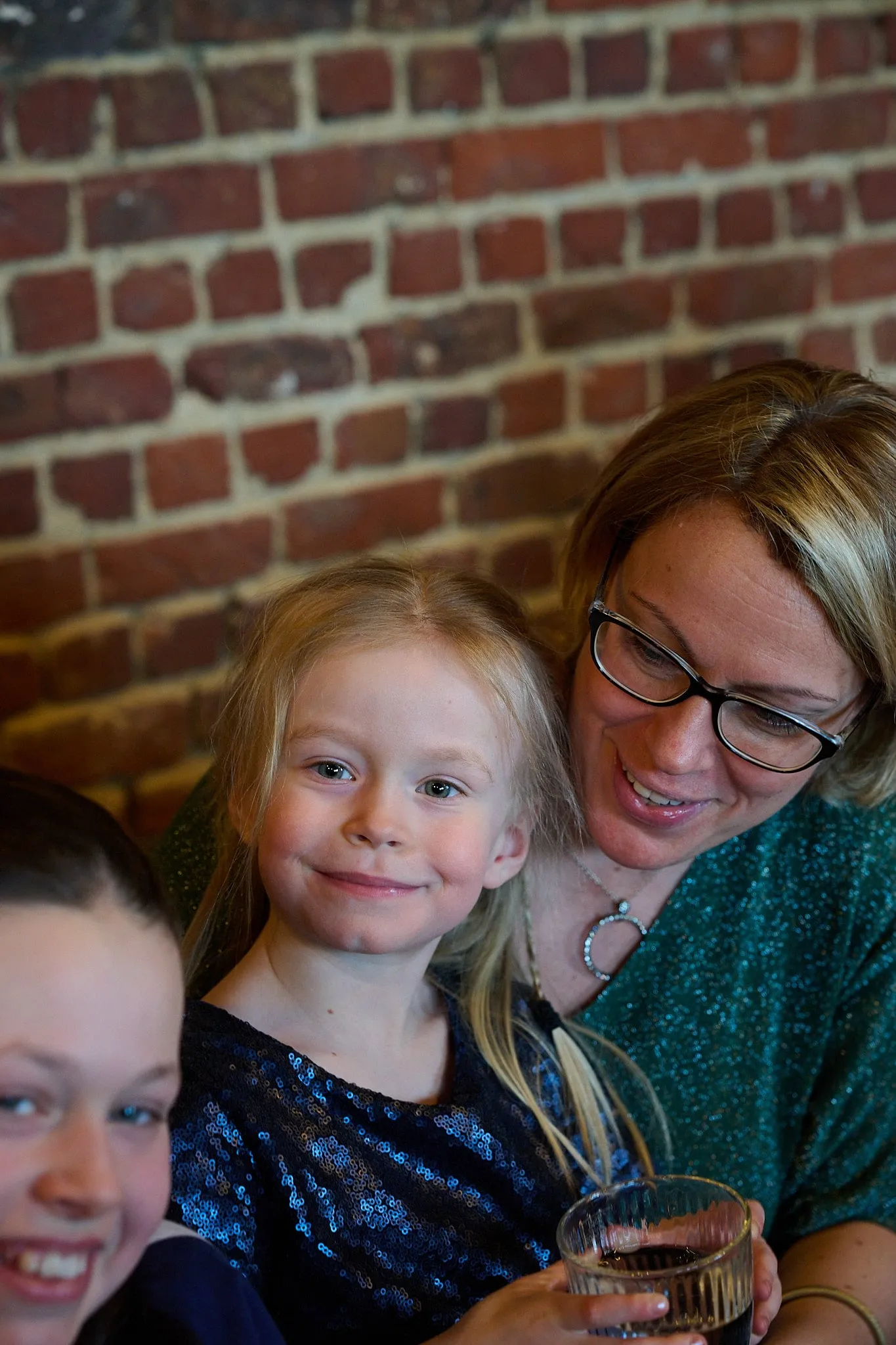 Meisje en vrouw met bril poseren voor een bakstenen muur