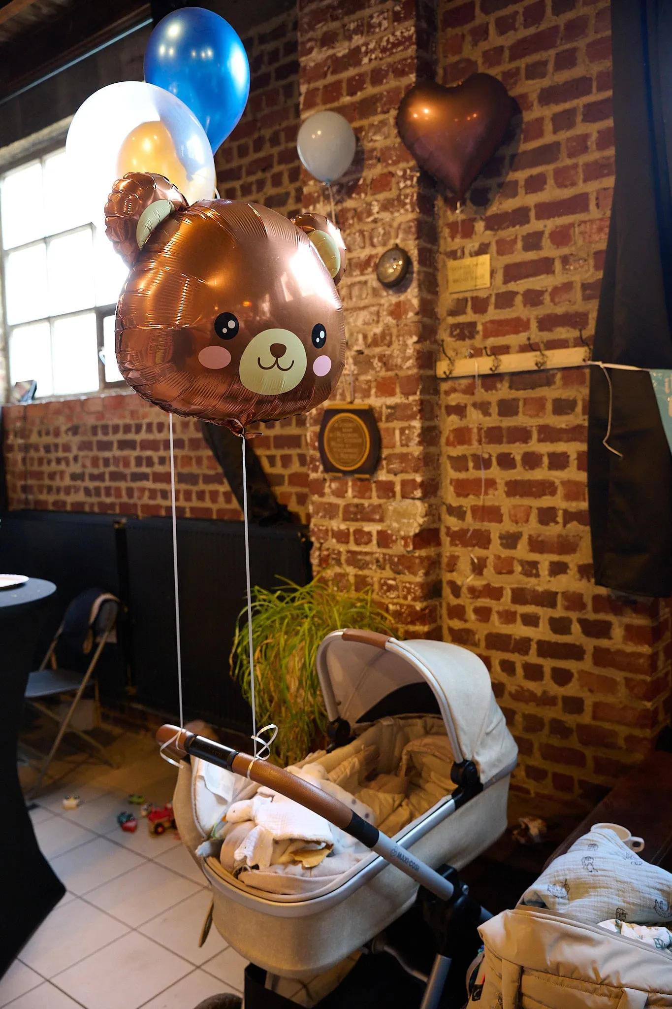 Teddybeerballon, ballonnen en een kinderwagen bij een bakstenen muur