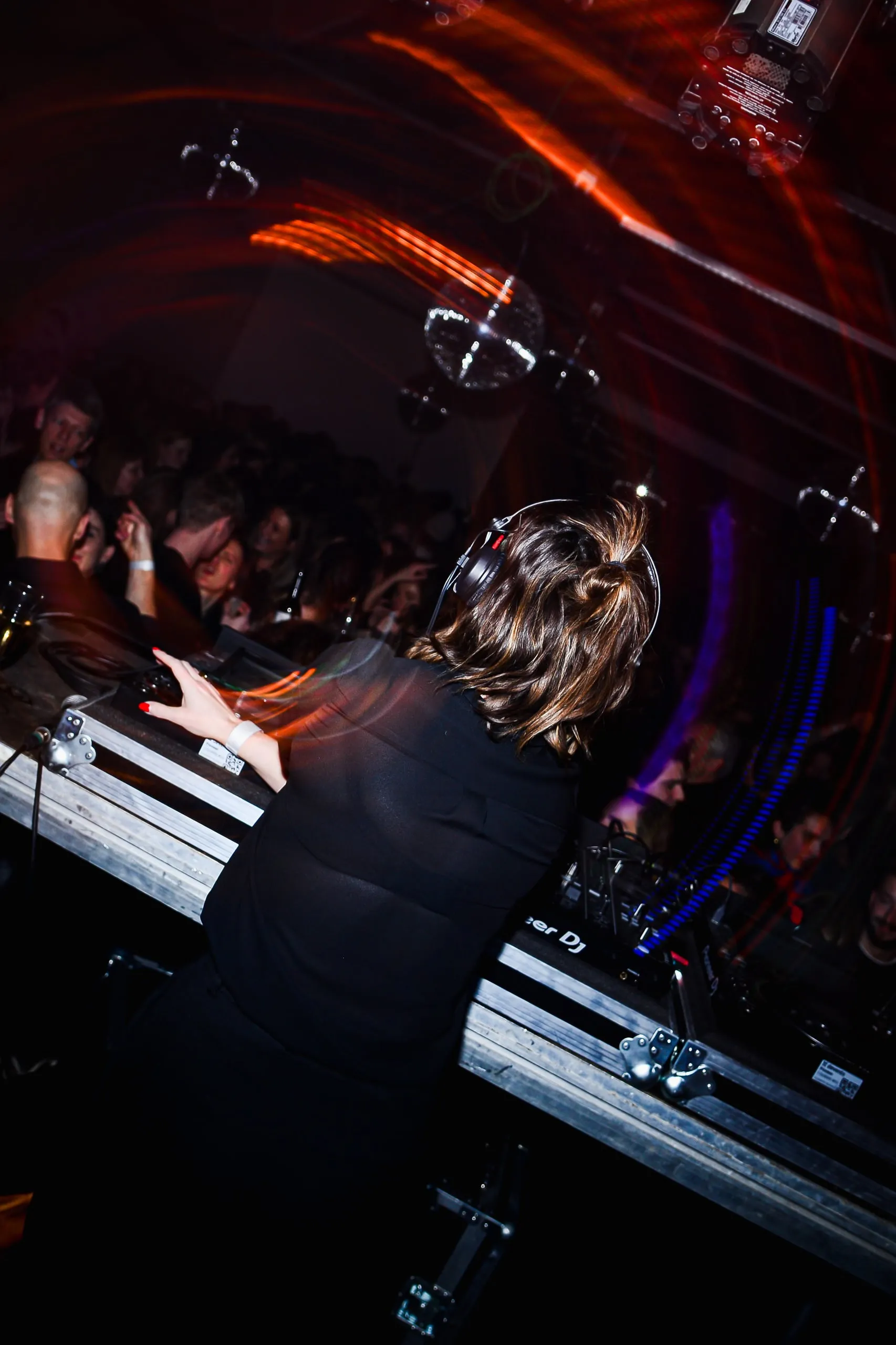 DJ achter de draaitafels, van achteren gezien, met rode lichtsporen