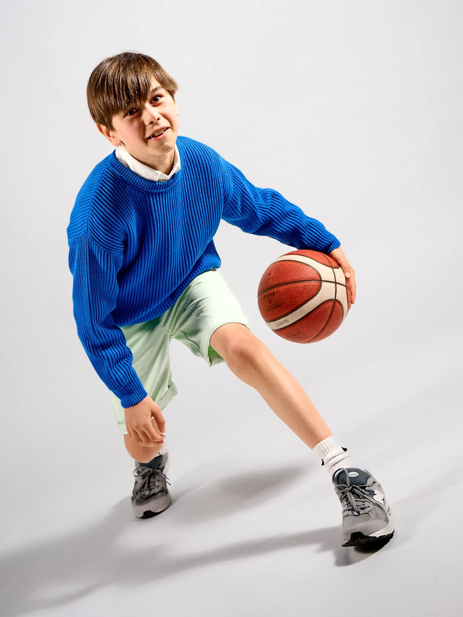 Jongen in blauwe trui dribbelt met een basketbal in de studio