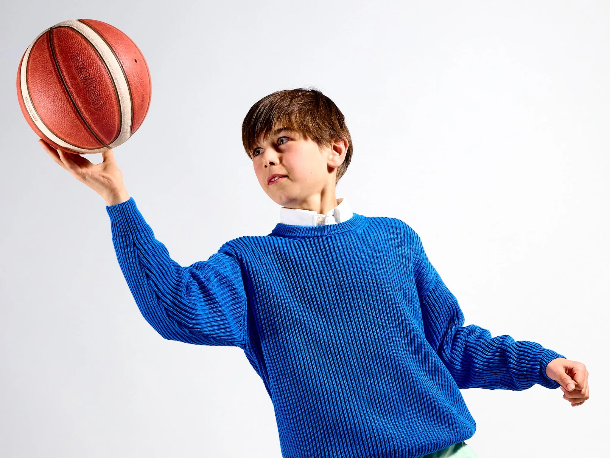 Jongen in blauwe trui houdt een basketbal omhoog