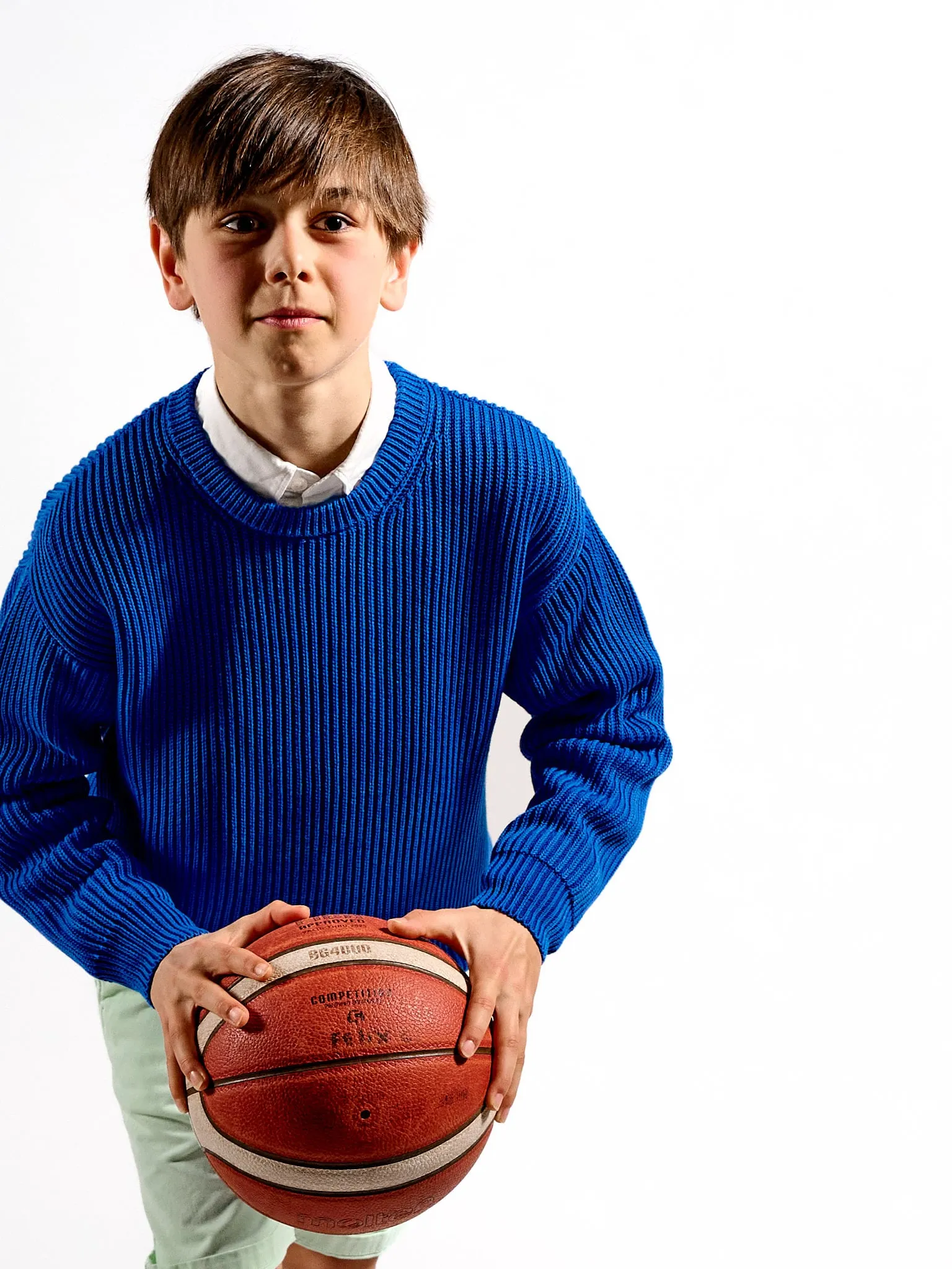 Jongen in blauwe trui houdt een basketbal vast voor een witte achtergrond