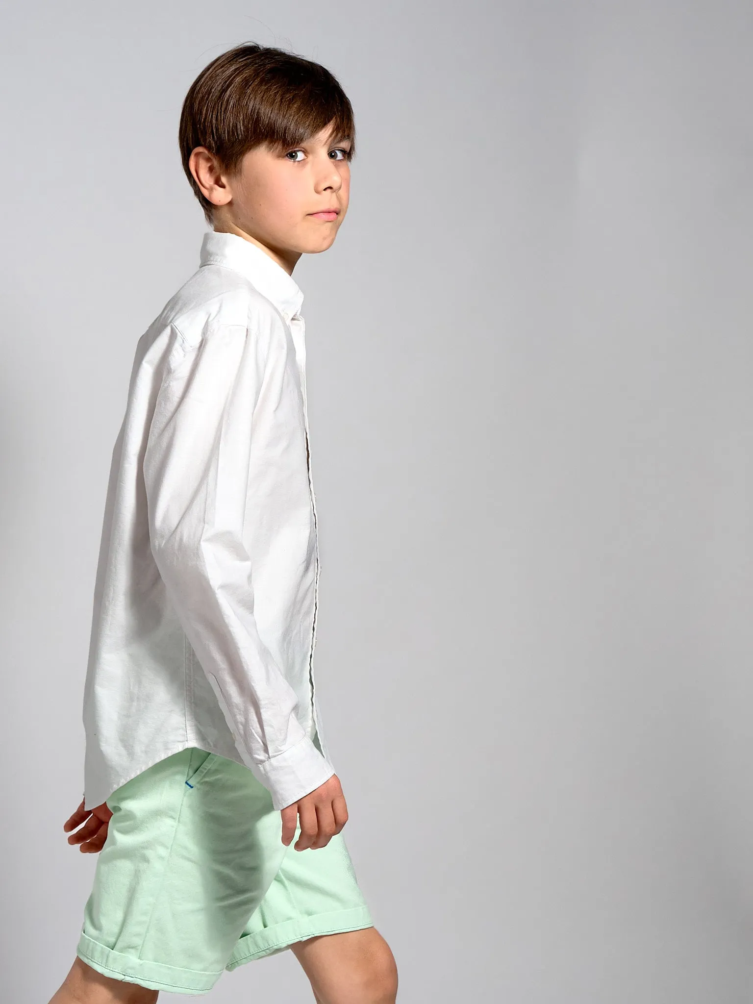 Jongen in wit hemd en lichtgroene short loopt in profiel