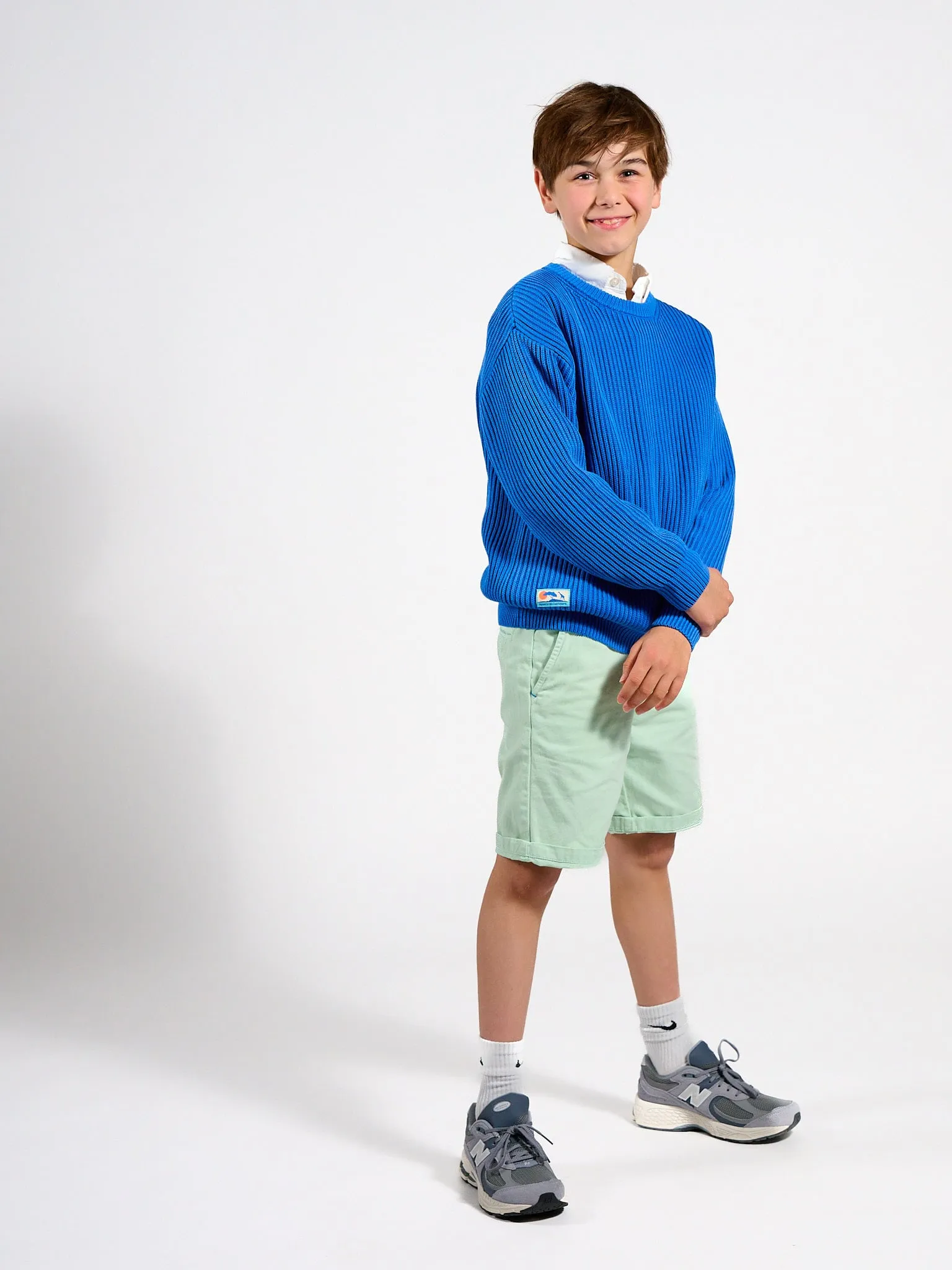 Lachende jongen in blauwe trui en lichtgroene short, volledige figuur