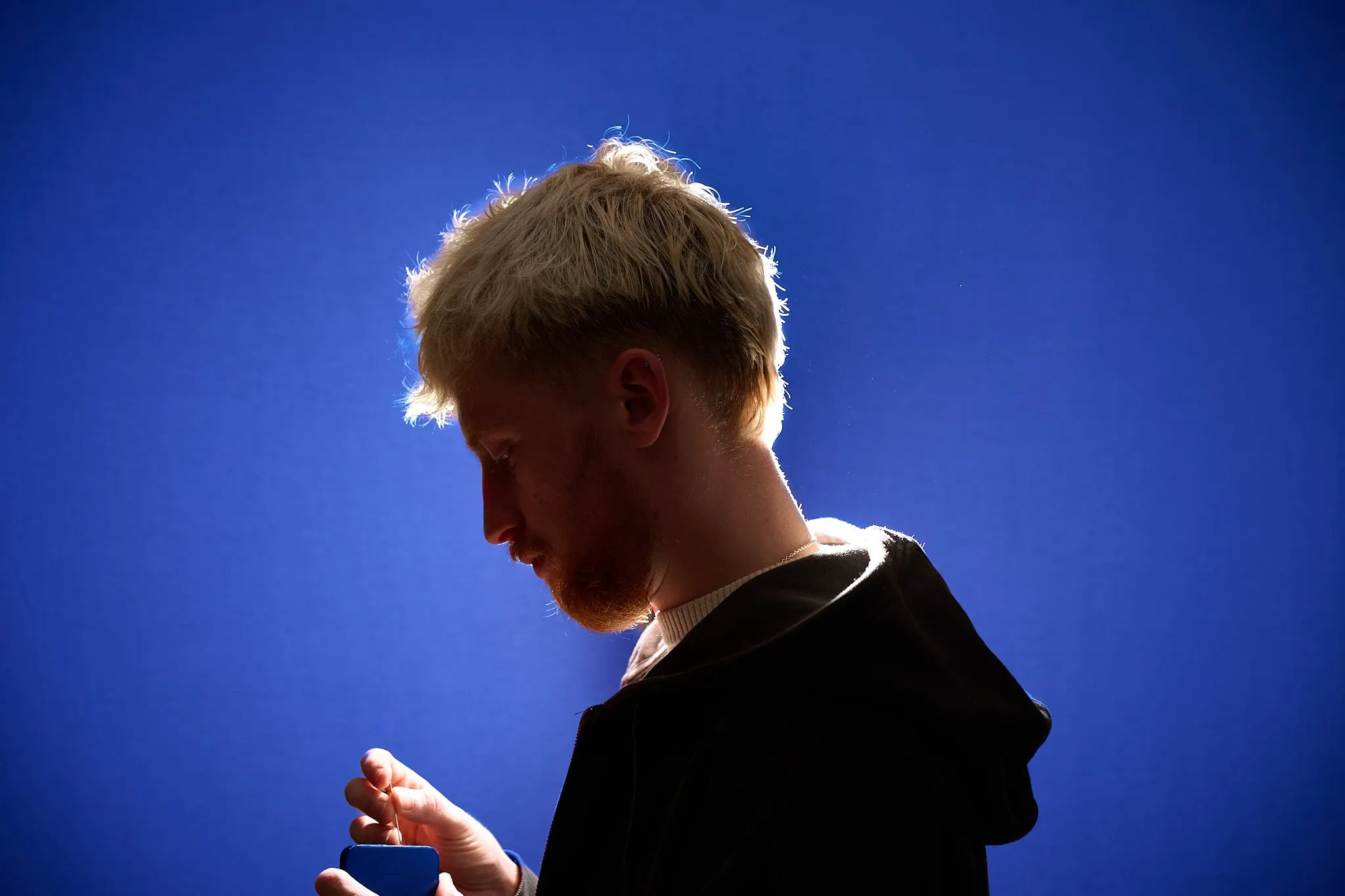 Man met blond haar in profiel voor een felblauwe achtergrond