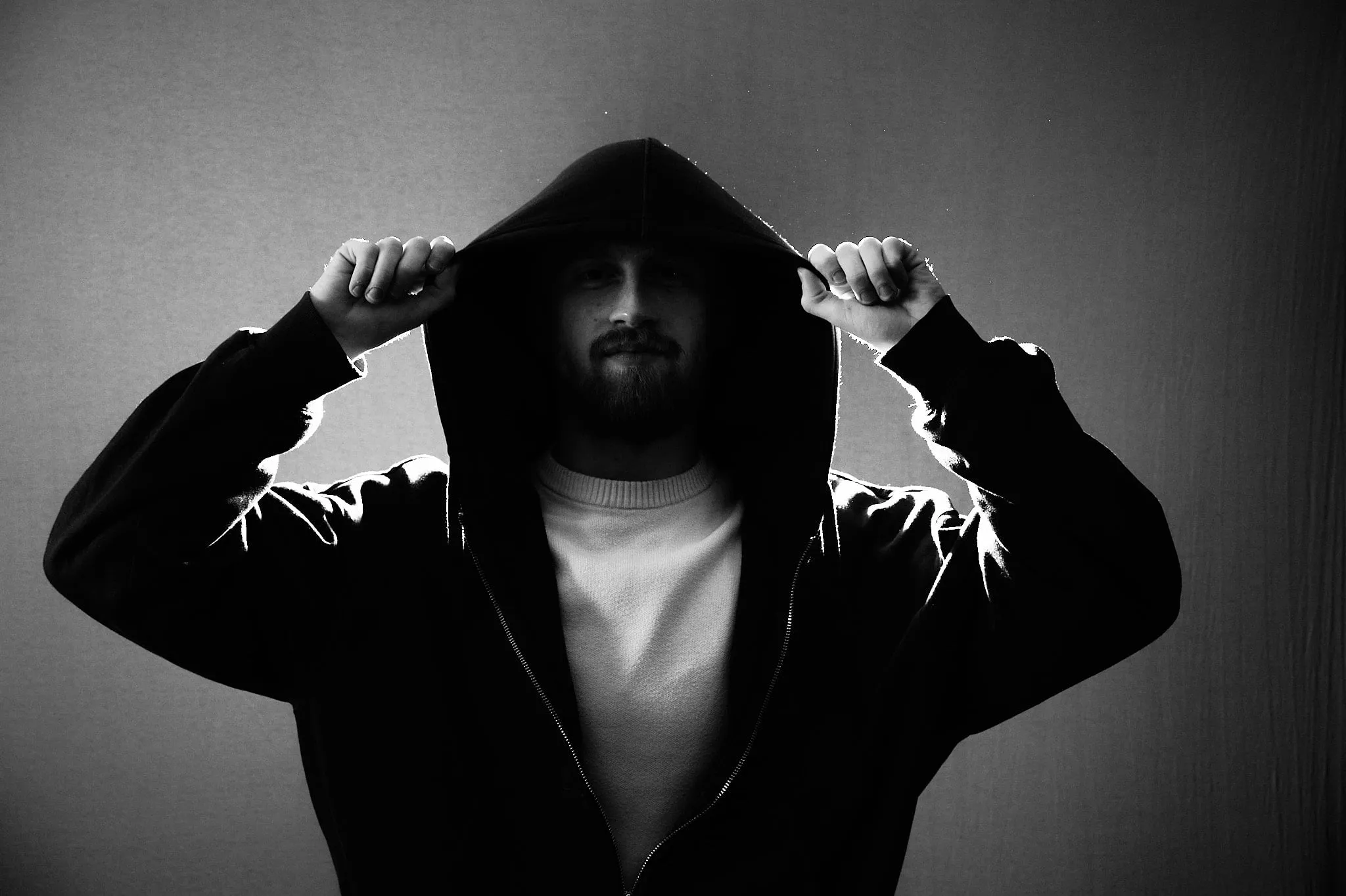 Man in zwarte hoodie trekt de capuchon op, met tegenlicht, in zwart-wit