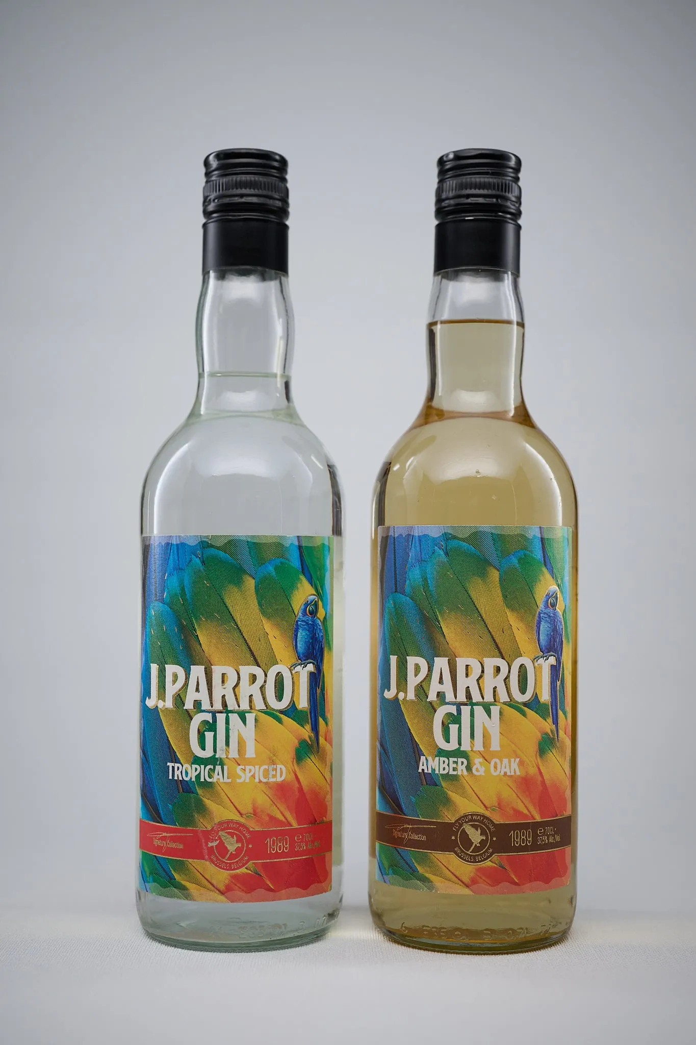 Twee flessen J. Parrot Gin (Tropical Spiced en Amber & Oak) tegen een lichtgrijze achtergrond