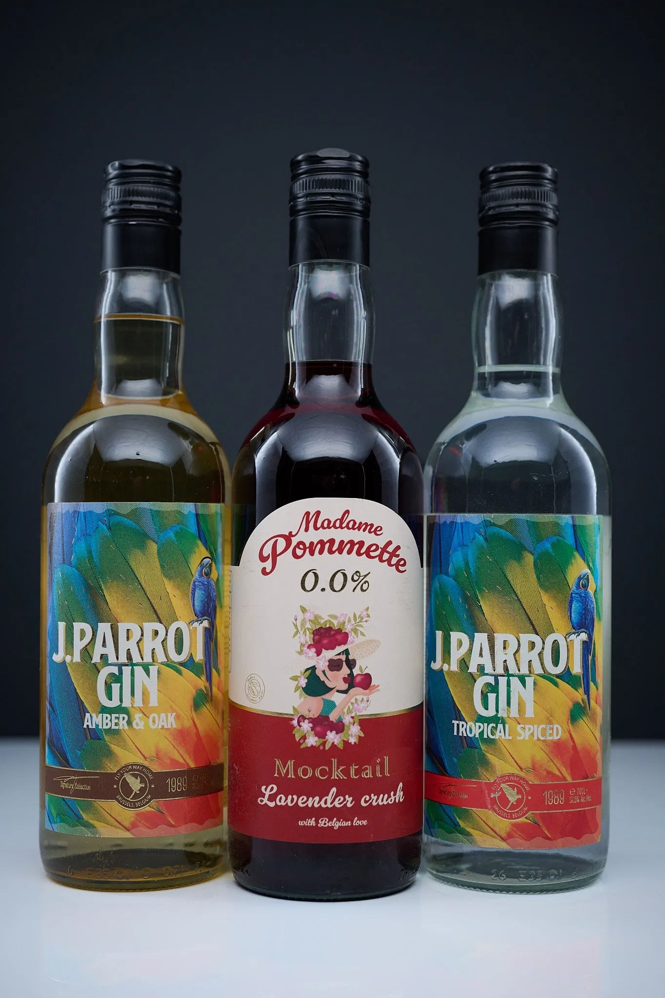 Drie flessen J. Parrot Gin en Madame Pommette naast elkaar voor een donkere achtergrond