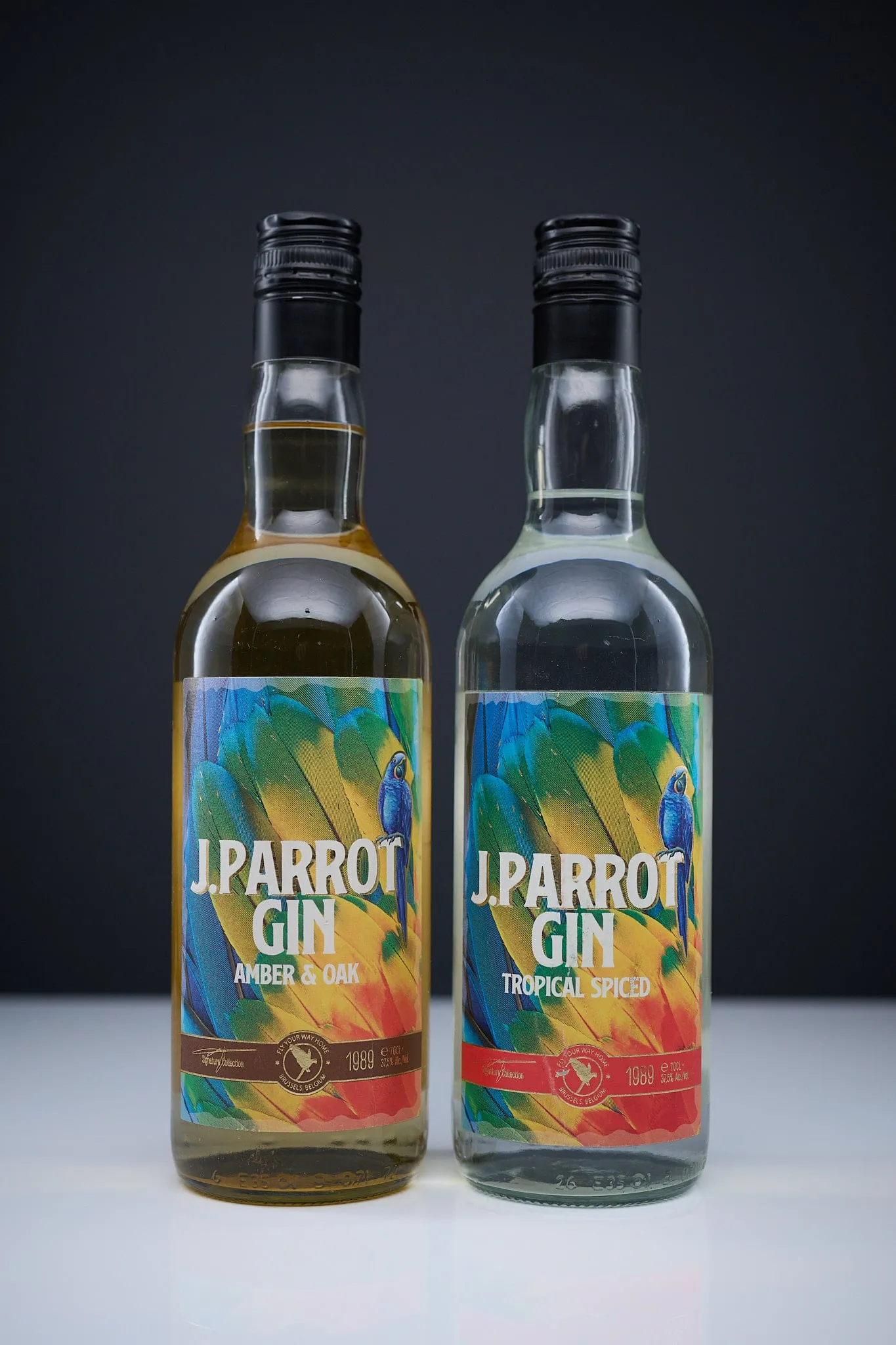 Twee flessen J. Parrot Gin, Amber & Oak en Tropical Spiced, voor een donkere achtergrond